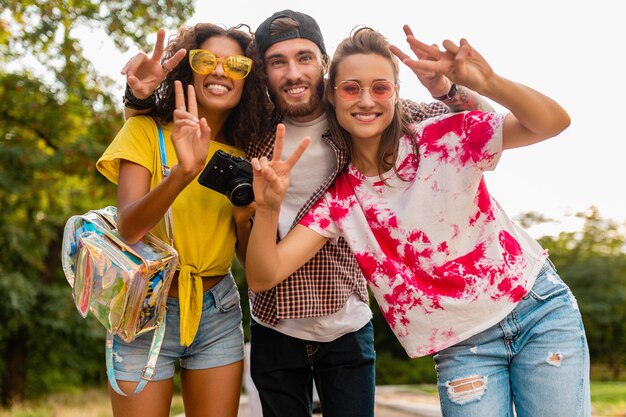 Glückliche junge Gesellschaft von emotional lächelnden Freunden, die im Park mit Fotokamera, Mann und Frauen gehen, die Spaß zusammen haben