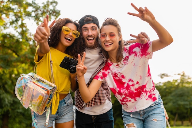 Glückliche junge Gesellschaft von emotional lächelnden Freunden, die im Park mit Fotokamera, Mann und Frauen gehen, die Spaß zusammen haben