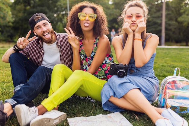 Glückliche junge Gesellschaft von Freunden, die Park sitzen, Mann und Frauen, die Spaß zusammen haben, mit Kamera reisen, lustig emotional