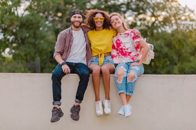 Glückliche junge Gesellschaft von lächelnden Freunden, die im Park sitzen, Mann und Frauen, die Spaß zusammen haben