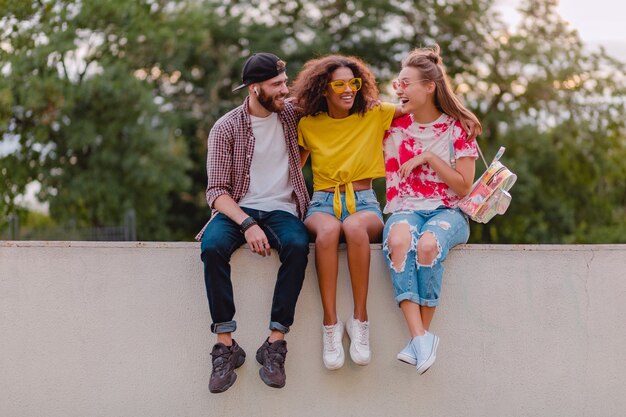 Glückliche junge Gesellschaft von lächelnden Freunden, die im Park sitzen, Mann und Frauen, die Spaß zusammen haben