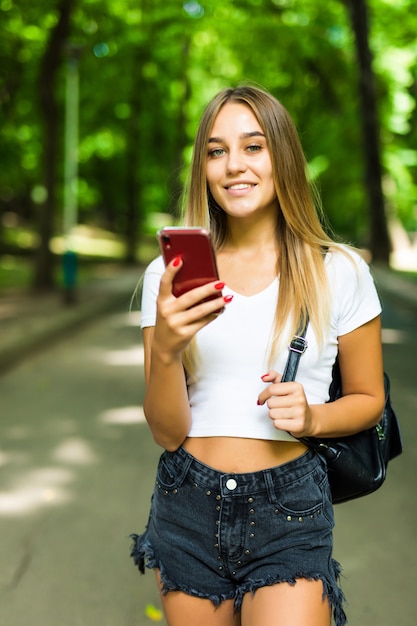 Glückliche junge hübsche Frau draußen im Park unter Verwendung des Mobiltelefons.