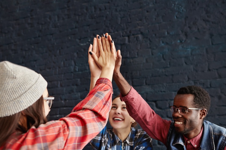 Kostenlose Foto glückliche junge leute, die high five geben und sich gegenseitig die hand gratulieren, gratulieren während des treffens im café. kreative unternehmer in informeller kleidung lachen und feiern den erfolg des start-up-projekts