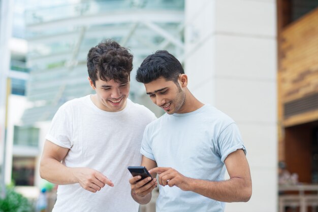 Glückliche junge Männer, die Smartphone beim Prüfen der neuen Anwendung verwenden