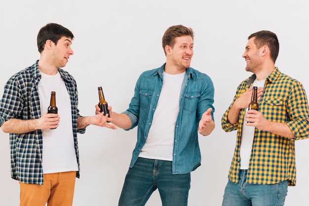 Glückliche junge männliche Freunde, welche die Bierflasche in der Hand macht Spaß gegen weißen Hintergrund halten