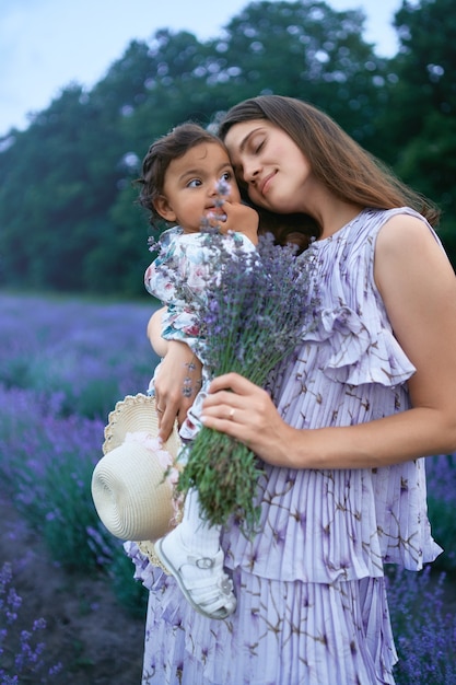 Glückliche junge Mutter, die Lavendelblumenstrauß und -kind hält