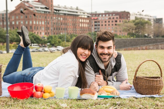 Glückliche junge Paare, die auf Decke mit vielem gesundem Snack im Picknick liegen