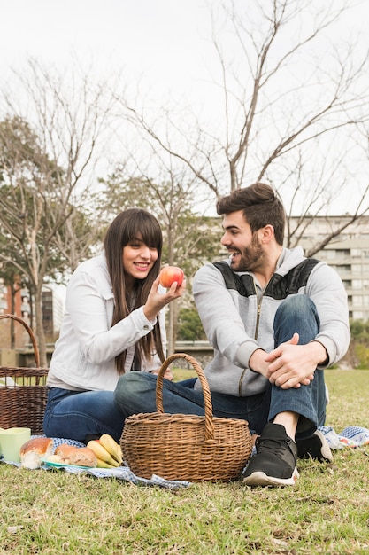 Glückliche junge Paare, die roten Apfel im Park betrachten