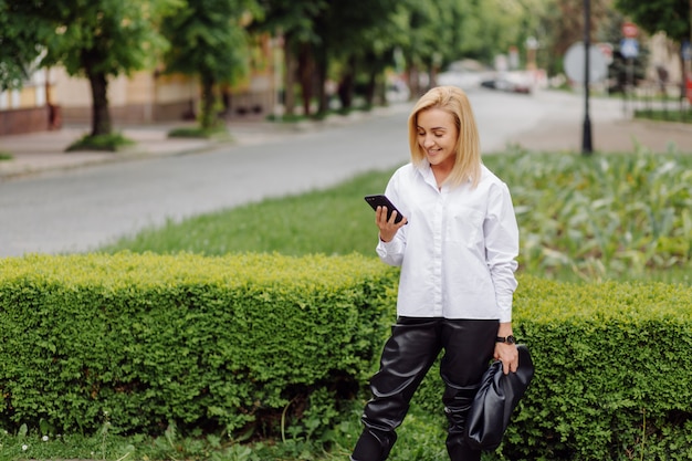 Glückliche junge schöne Frau mit ihrem Smartphone, das auf der Stadtstraße geht