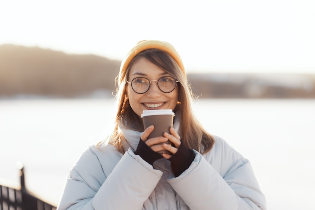 Glückliche junge Teenagerfrau, die eine Kaffeetasse zum Mitnehmen hält