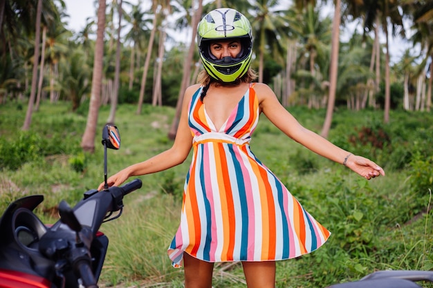 Glückliche kaukasische Bikerfrau im bunten Sommerkleid im Urlaub mit Motorradhelm