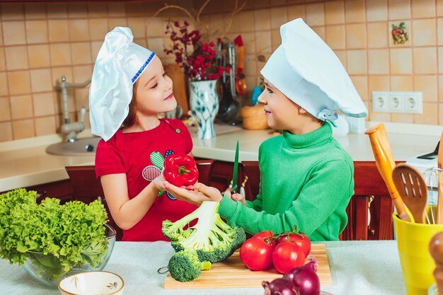 Glückliche Kinder bereiten frischen Gemüsesalat in der Küche zu