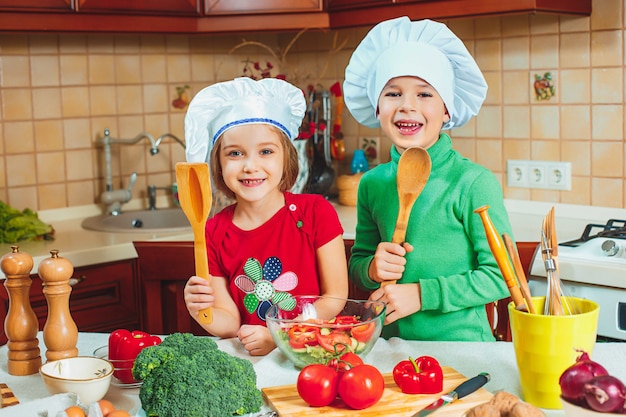 Glückliche Kinder bereiten frischen Gemüsesalat in der Küche zu