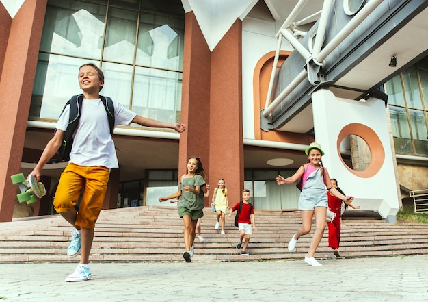 Glückliche Kinder, die an der Straße der Stadt am sonnigen Sommertag vor dem modernen Gebäude spielen. Gruppe von glücklichen Kindern oder Jugendlichen, die Spaß zusammen haben. Konzept der Freundschaft, Kindheit, Sommer, Ferien.