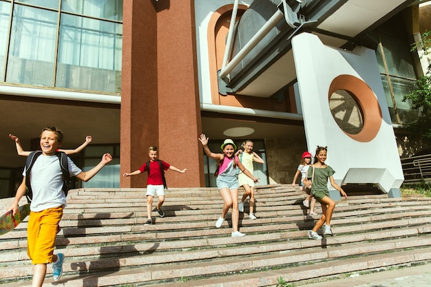 Kostenloses Foto glückliche kinder, die an der straße der stadt am sonnigen sommertag vor dem modernen gebäude spielen. gruppe von glücklichen kindern oder jugendlichen, die spaß zusammen haben. konzept der freundschaft, kindheit, sommer, ferien.