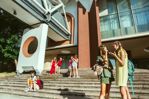 Kostenloses Foto glückliche kinder, die an der straße der stadt am sonnigen sommertag vor dem modernen gebäude spielen. gruppe von glücklichen kindern oder jugendlichen, die spaß zusammen haben. konzept der freundschaft, kindheit, sommer, ferien.