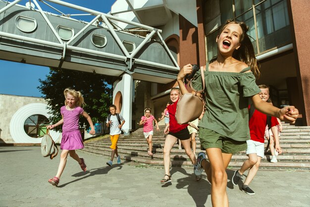 Glückliche Kinder, die an der Straße der Stadt am sonnigen Sommertag vor dem modernen Gebäude spielen. Gruppe von glücklichen Kindern oder Jugendlichen, die Spaß zusammen haben