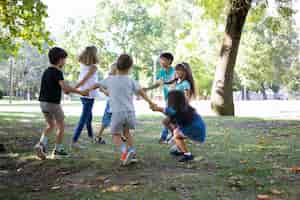 Kostenloses Foto glückliche kinder, die zusammen draußen spielen, auf gras tanzen, aktivitäten im freien genießen und spaß im park haben. kinderparty oder freundschaftskonzept
