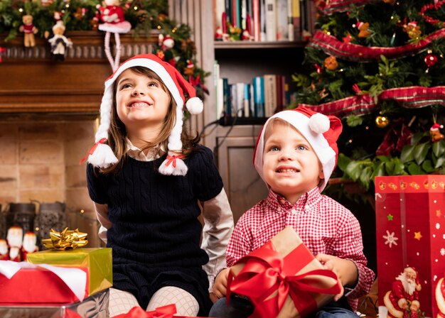 Glückliche Kinder in einem Wohnzimmer auf Weihnachten sitzen