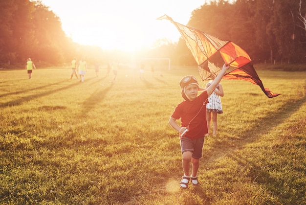 Glückliche Kinder starten bei Sonnenuntergang einen Drachen auf dem Feld. Kleiner Junge und Mädchen in den Sommerferien