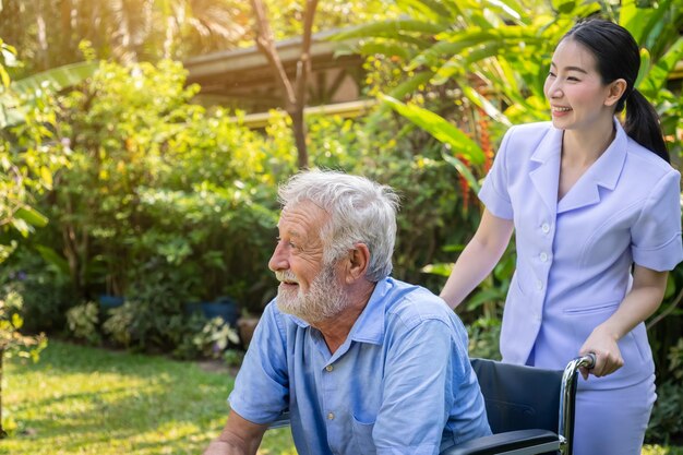 Glückliche Krankenschwester kümmert sich um älteren Mann im Rollstuhl im Garten des Pflegeheims