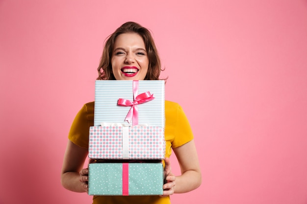 Glückliche lachende Frau mit roten Lippen, die Bündel von Geschenkboxen halten,