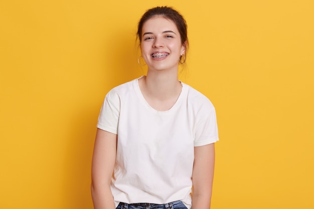 Glückliche lächelnde brünette junge Frau mit Haarknoten kleidet weißes lässiges T-Shirt, posierend