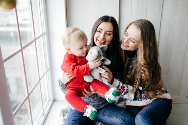 Glückliche lächelnde Familie am Studio auf Hintergrund des Weihnachtsbaums mit Geschenk