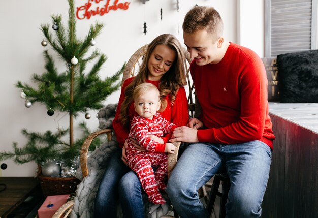 Glückliche lächelnde Familie am Studio auf Hintergrund des Weihnachtsbaums mit Geschenk