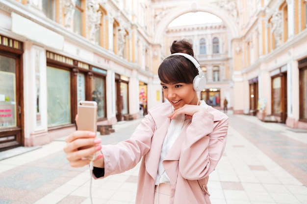 Glückliche lächelnde junge Frau in den Kopfhörern, die selfie Foto machen
