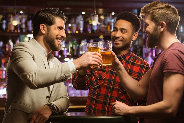 Glückliche lächelnde männliche Freunde, die mit Bierkrügen klirren