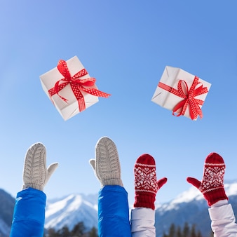 Glückliche leute werfen weihnachtsgeschenkbox gegen hintergrund des blauen himmels auf. glückliches paar, das im winter spaß im freien hat. weihnachtsferienkonzept