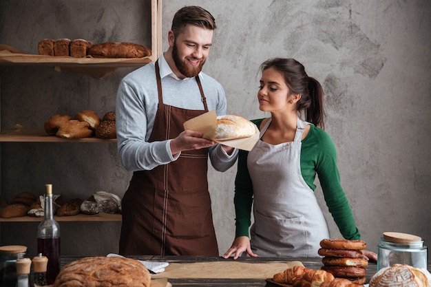 Glückliche liebende Paarbäcker, die an Bäckerei stehen, die Brot hält