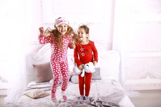 Glückliche lustige Kinder in hellen Pyjamas springen auf das Bett und spielen zusammen
