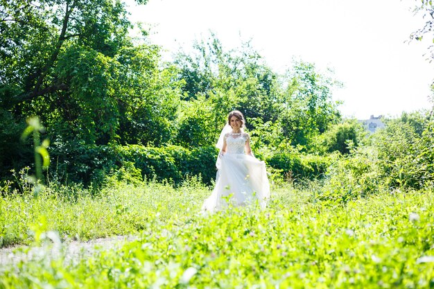 Glückliche mädchenbraut in einem langen weißen hochzeitskleid und in einem schleierwirbel in einem grünen park auf natur.
