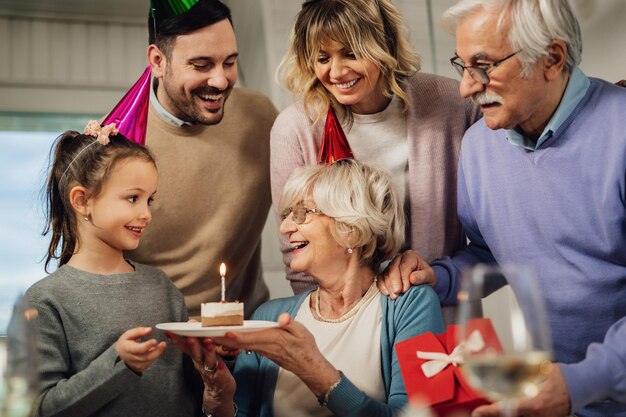 Glückliche Mehrgenerationenfamilie, die Spaß hat, während sie Seniorin an ihrem Geburtstag mit einem Kuchen überrascht