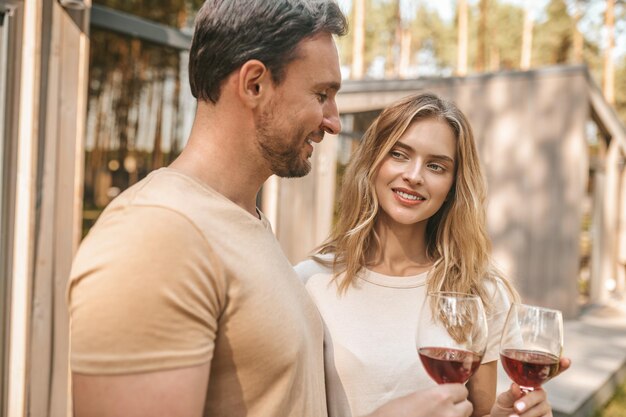 Glückliche Momente. Junges lächelndes Paar, das Gläser mit Wein hält und glücklich schaut