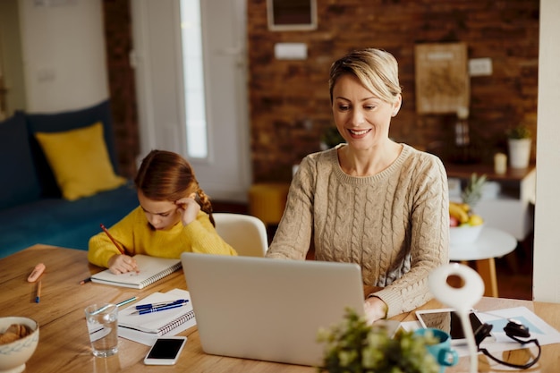 Glückliche Mutter, die Computer verwendet, während sie zu Hause arbeitet