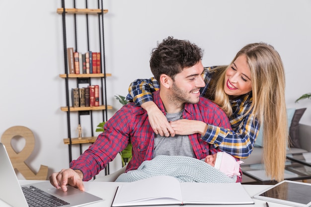 Glückliche Mutter, die Vater mit Baby am Schreibtisch umarmt