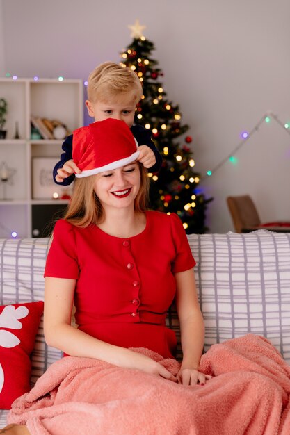 Glückliche Mutter im roten Kleid sitzt auf einer Couch lächelnd, während ihr kleines Kind