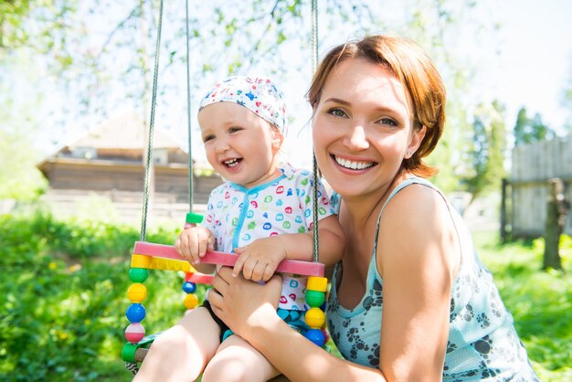 Glückliche Mutter mit lachendem Baby sitzt auf der Schaukel