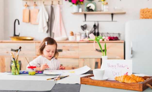 Glückliche Mutter-Tagesaufschrift auf Tabelle nahe malendem Mädchen
