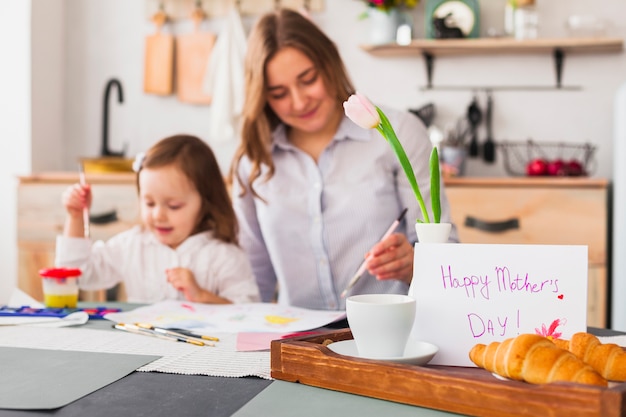 Glückliche Mutter-Tagesaufschrift auf Tabelle nahe malender Tochter und Mutter