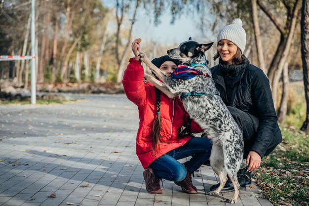 Glückliche Mutter und ihre Tochter spielen mit Hund im Herbstpark