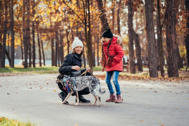 Glückliche Mutter und ihre Tochter spielen mit Hund im Herbstpark