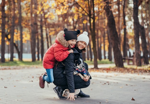 Glückliche Mutter und ihre Tochter spielen mit Hund im Herbstpark