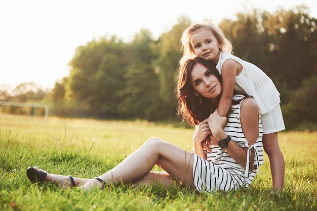 Glückliche Mutter und Tochter, die in einem Park in der Sonne an einem hellen Sommer der Kräuter umarmen.