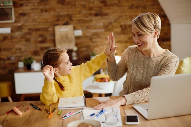 Glückliche Mutter und Tochter, die während des Homeschooling Highfive geben