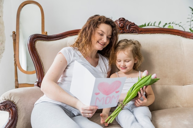 Kostenloses Foto glückliche mutter- und tochterlesegrußkarte zusammen im haus mit tulpenblumen