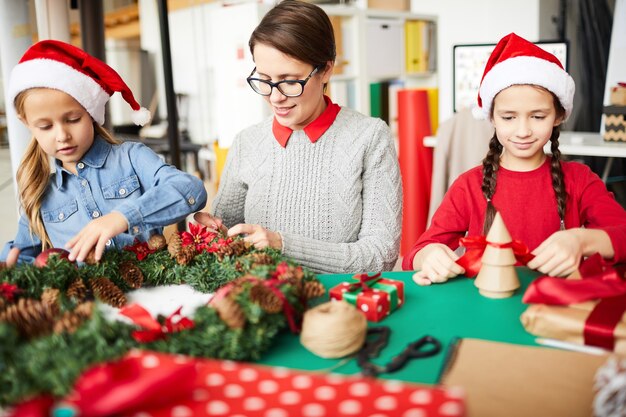 Glückliche Mutter und Töchter, die den Weihnachtskranz schmücken